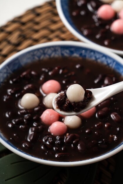 Cerca de tangyuan rojo y blanco (tang yuan, bolas de bola de masa de arroz glutinoso) con sopa de frijoles rojos dulces en un recipiente sobre fondo blanco de mesa para la comida del festival del solsticio de invierno.