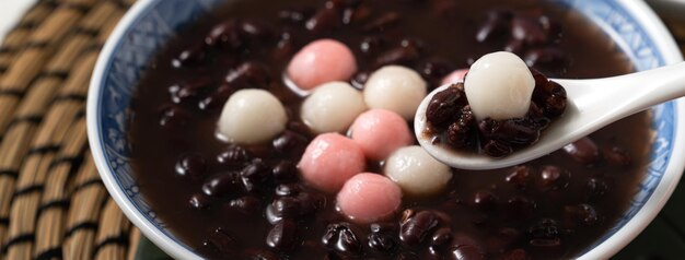 Cerca de tangyuan rojo y blanco (tang yuan, bolas de bola de masa de arroz glutinoso) con sopa de frijoles rojos dulces en un recipiente sobre fondo blanco de mesa para la comida del festival del solsticio de invierno.