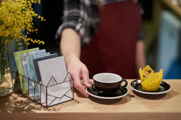 cerca de una taza de café en un estante de café con un pastelito, flores de mimosa y calendarios.