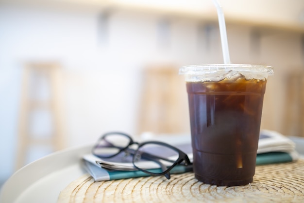 Cerca de la taza de plástico para llevar de café negro helado Americano en mesa redonda