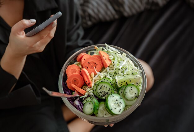 Cerca de un tazón grande con ensalada de verduras recién preparada en manos femeninas.