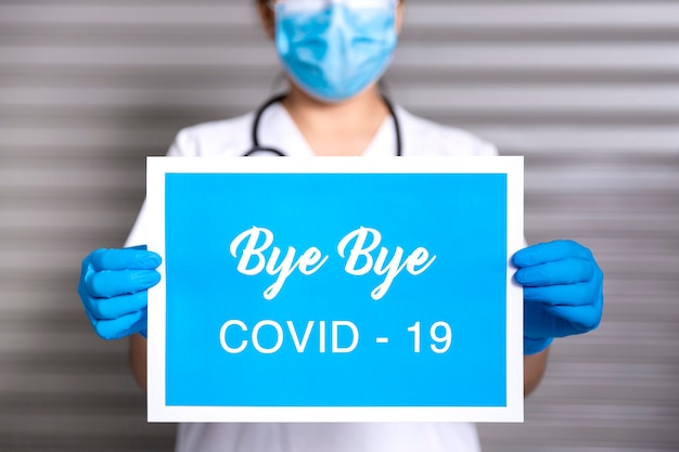 Cerca del trabajador de la salud con una máscara y guantes protectores sosteniendo un cartel con el texto Bye Bye Covid19