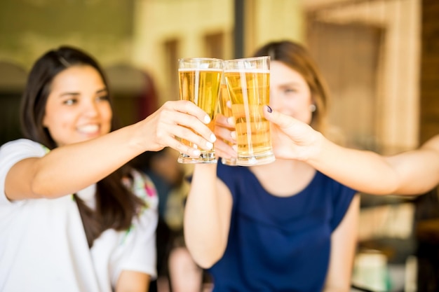 Cerca de tres mujeres brindando vasos de cerveza en el restaurante