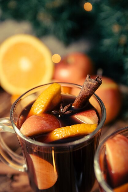 Cerca de vino caliente de Navidad con frutas y especias en mesa de madera