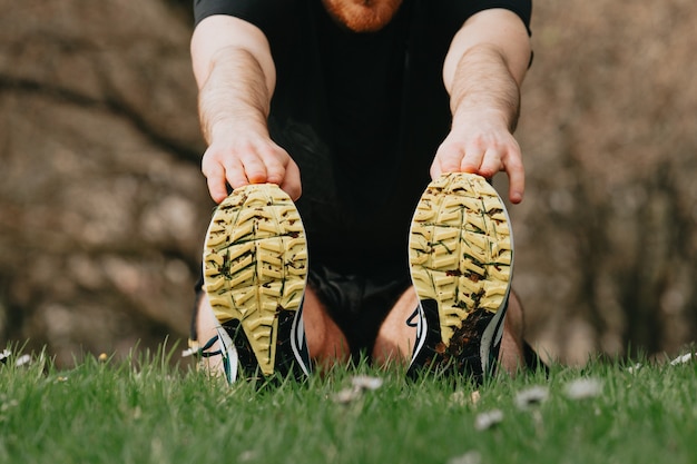 Foto cerca de los zapatos de entrenamiento mientras estira las piernas sobre el césped del parque