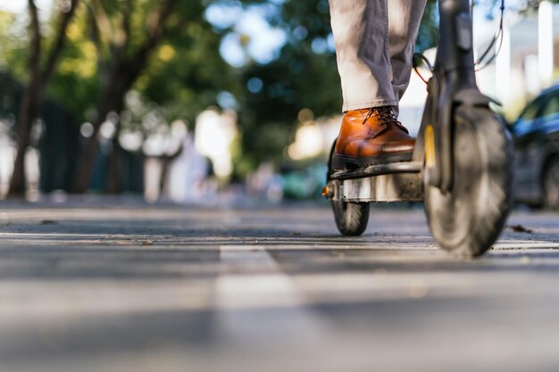 Cerca de los zapatos de un hombre que monta un scooter eléctrico por la ciudad