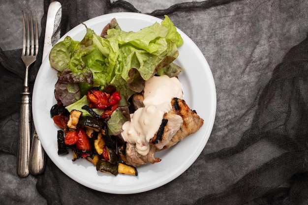 Cerdo al horno con verduras y ensalada fresca en plato blanco