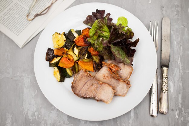 Cerdo al horno con verduras y ensalada fresca en plato blanco