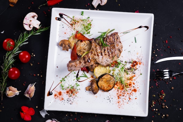 Cerdo asado con verduras asadas sobre una superficie oscura