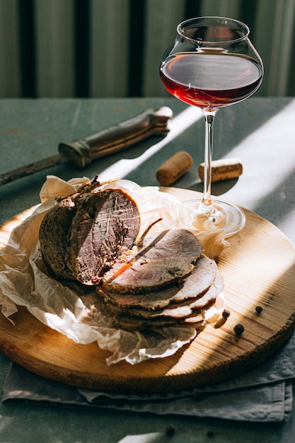 Foto cerdo cocido al horno con ajo y especias con vino tinto en un vaso sobre una bandeja de madera, fondo gris