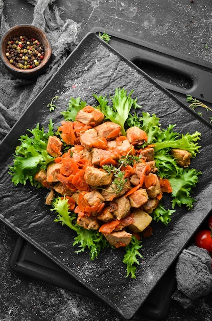 Cerdo guisado con verduras en cerveza sobre un plato de piedra negra Vista superior Sobre un fondo negro