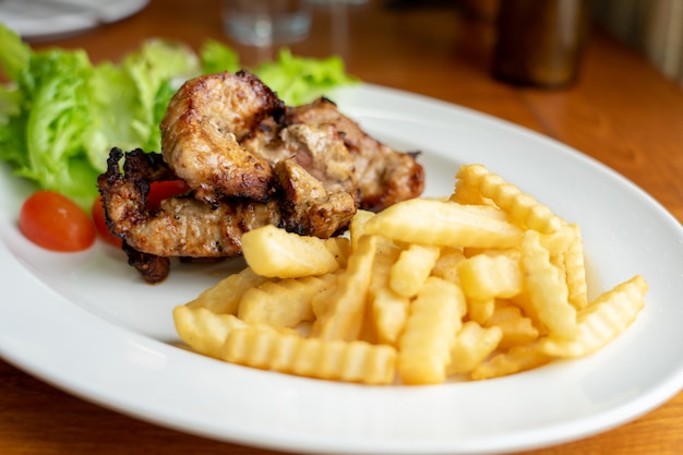 Cerdo a la parrilla y papas fritas, dispuestas en un hermoso plato de comida blanca con ensalada