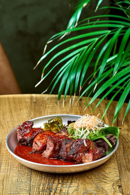 Cerdo a la parrilla con salsa barbacoa roja pepinos ponzu y salsa en un plato sobre un fondo de madera