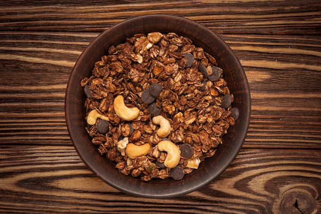 Cereais de granola de chocolate com nozes em uma tigela na parede de madeira.