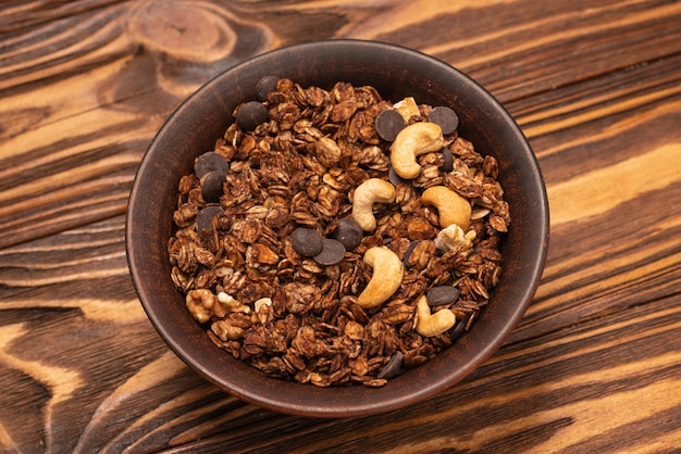 Cereais de granola de chocolate com nozes em uma tigela sobre uma superfície de madeira.