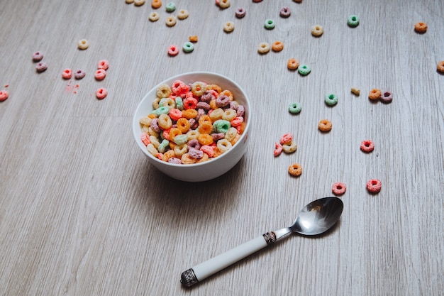 Cereal de colores en un cuenco con cuchara en el suelo.