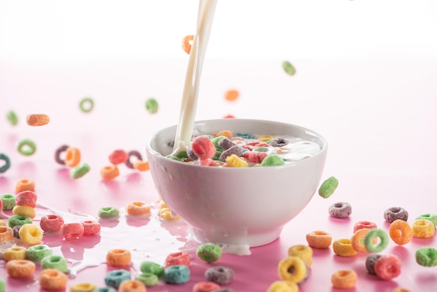 Cereal de café da manhã multicolorido brilhante na tigela com leite derramado no fundo rosa