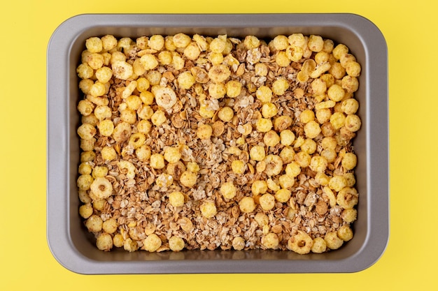 Cereal de granola crocante torrado caseiro orgânico com flocos de aveia e linhaça e bolas de milho crocantes e anéis na assadeira em fundo amarelo brilhante Vista superior plana leiga muesli