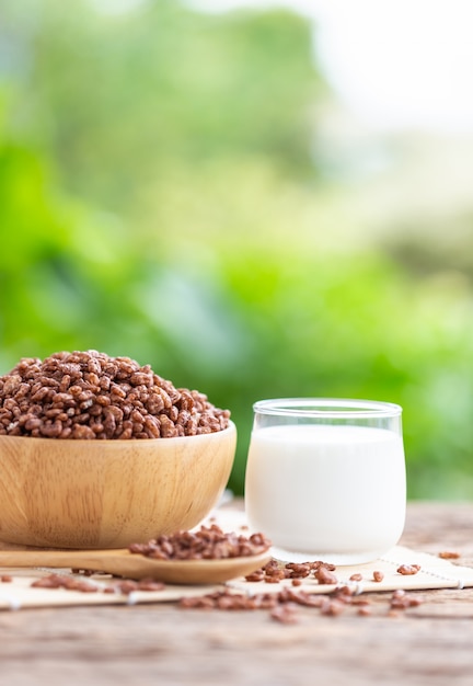 Cereal de desayuno, arroz inflado con cacao en un tazón y vaso de leche en la mesa de madera