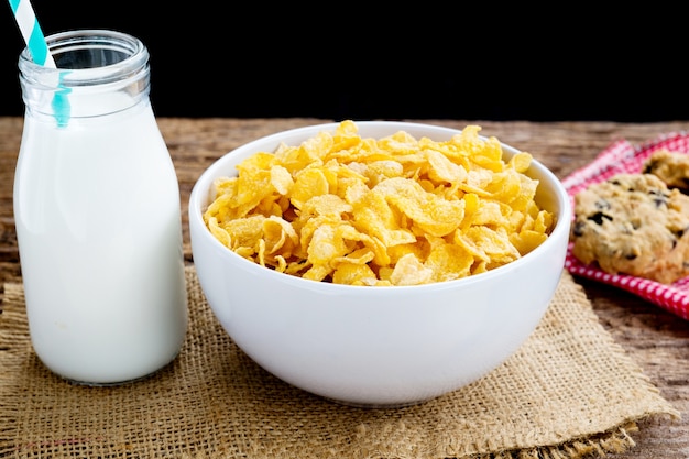 Cereales de copo de maíz en el cuenco blanco con el vidrio de leche en la tabla.