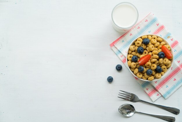 Cereales con desayuno de arándanos, leche y miel sobre un fondo blanco