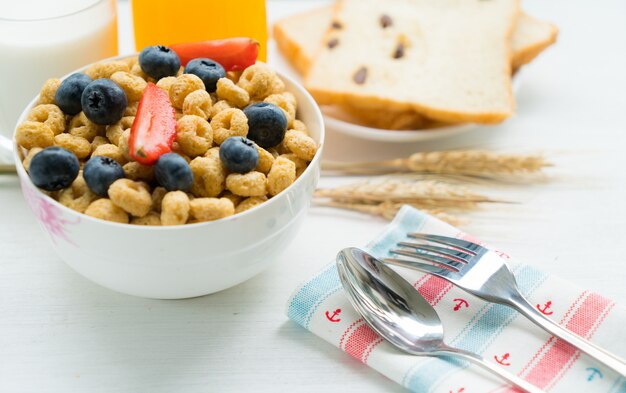 Cereales con desayuno de arándanos, leche y miel sobre un fondo blanco