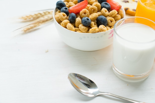 Cereales con desayuno de arándanos, leche y miel sobre un fondo blanco