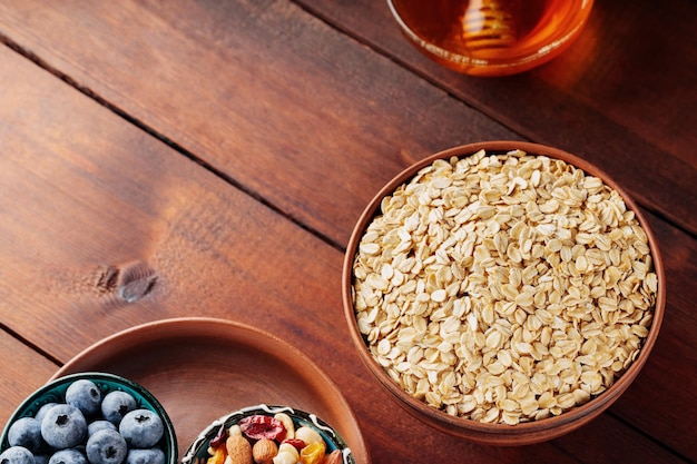 Cereales y diversos ingredientes deliciosos para el desayuno en tablas de madera. Copos de avena seca, arándanos, miel y frutos secos variados sobre un fondo de madera. Copie el espacio. Vista superior