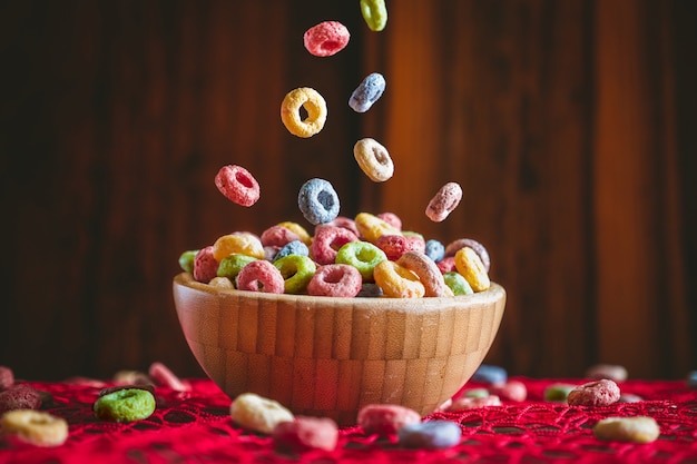 Cereales de frutas redondos coloridos cayendo en un recipiente de madera sobre una mesa roja