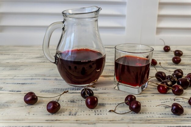 cereja e suco de cereja ou vinho em uma mesa de madeira um decantador e um copo com suco