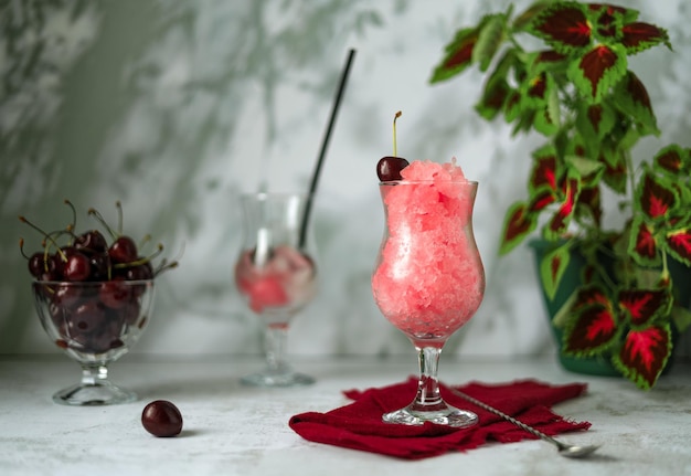 Cereja granita, bagas em um vaso de vidro e bebida refrescante com gelo sobre fundo cinza claro