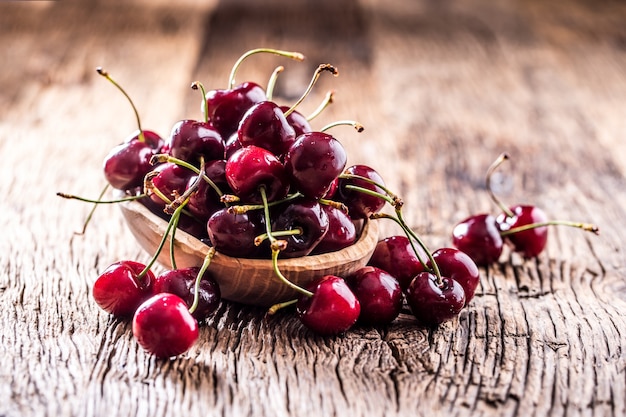 Cerejas Cerejas frescas. Deliciosas cerejas com água caem em uma tigela retrô na velha mesa de carvalho.