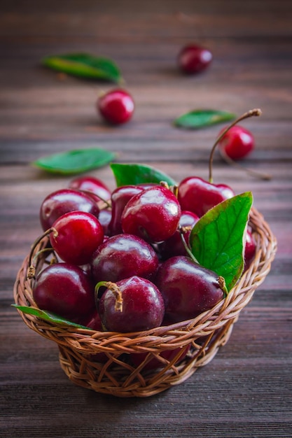 Cerejas com folhas em uma cesta em um fundo de madeira