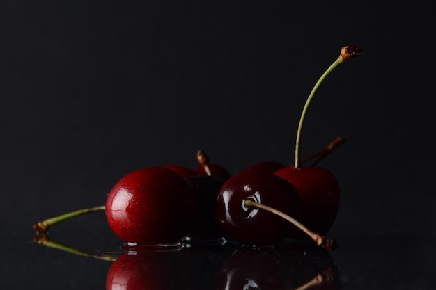 Cerejas, com gotas de água em um fundo preto com reflexo