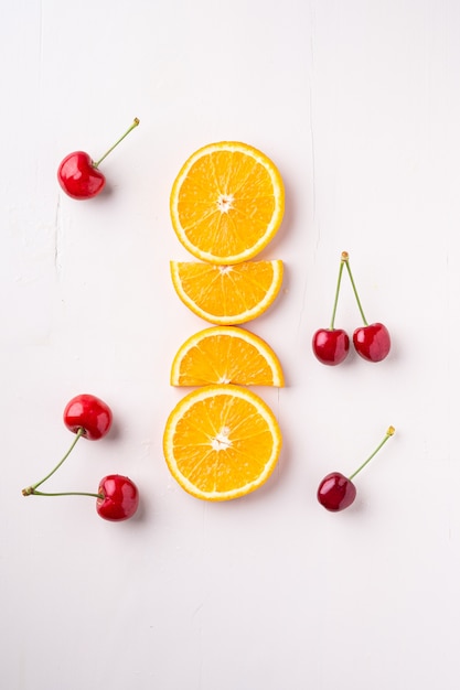 Cerejas de frutas de verão com laranjas em linha na vista superior, branca