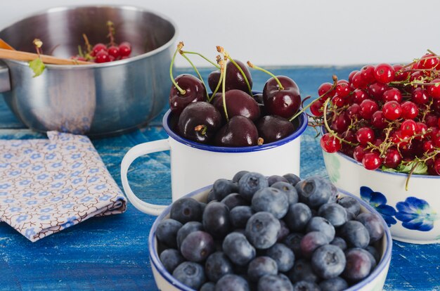 Cerejas e passas de Corinto dos cranberries na bacia branca no fundo de madeira envelhecido da cor azul.