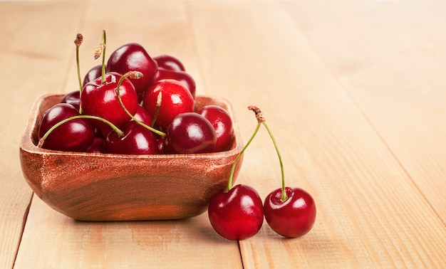 Cerejas frescas em um prato de madeira sobre a mesa