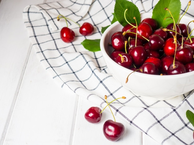Cerejas frescas em uma tigela branca sobre uma mesa de madeira branca
