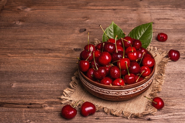 Cerejas frescas maduras em uma tigela com gotas de água. Fundo de madeira rústico escuro, espaço de cópia