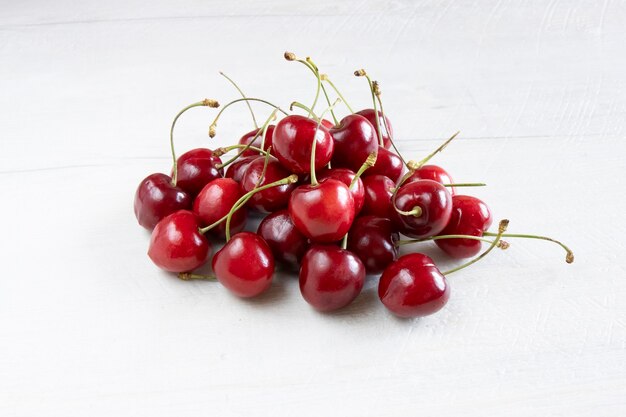 Foto cerejas lindas, frescas e suculentas na mesa de madeira branca.