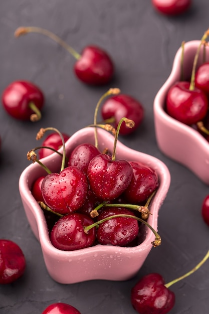 Cerejas maduras e suculentas em um prato rosa e dispersão, em forma de estrela. cinza, mesa de cimento. cartão postal