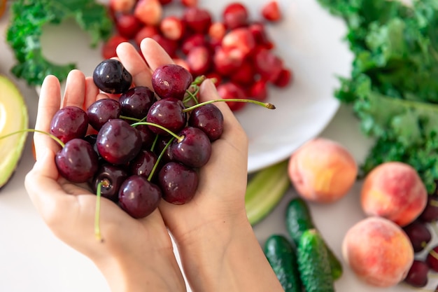 Cerejas maduras em mãos femininas em um fundo desfocado de frutas e legumes