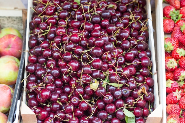 Cerejas suculentas brilhantes de diferentes tamanhos em caixas de madeira no mercado da cidade