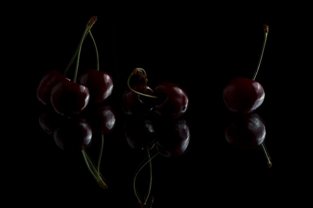 Cerejas vermelhas em um fundo branco com reflexão Cerejas frescas em um fundo preto