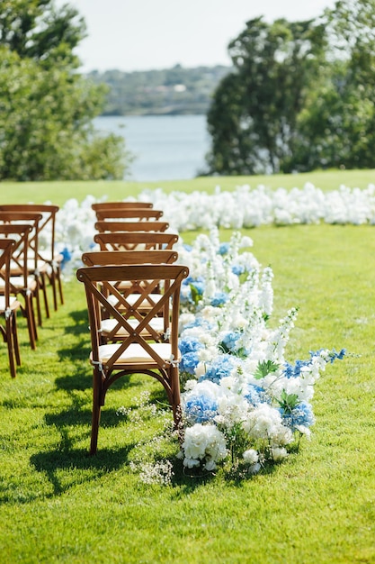 Ceremonia al aire libre increíblemente hermosa en pasto verde y sillas de madera y flores frescas el día de la boda