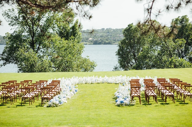 Ceremonia al aire libre increíblemente hermosa en pasto verde y sillas de madera y flores frescas el día de la boda