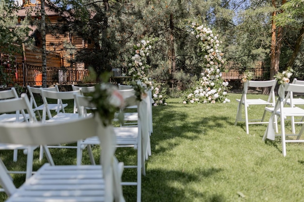 Foto ceremonia de boda al aire libre con un impresionante arco floral y sillas blancas en un jardín sereno