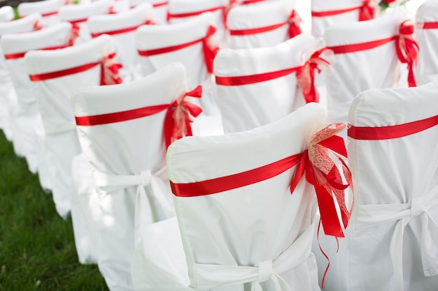 Ceremonia de boda al aire libre. Sillas blancas con cinta roja.