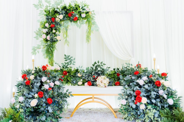 Una ceremonia de boda con una cortina blanca y un arco floral con rosas rojas y blancas y vegetación.