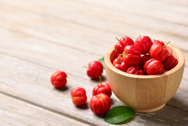 Cereza acerola en cuenco de madera sobre mesa de madera.